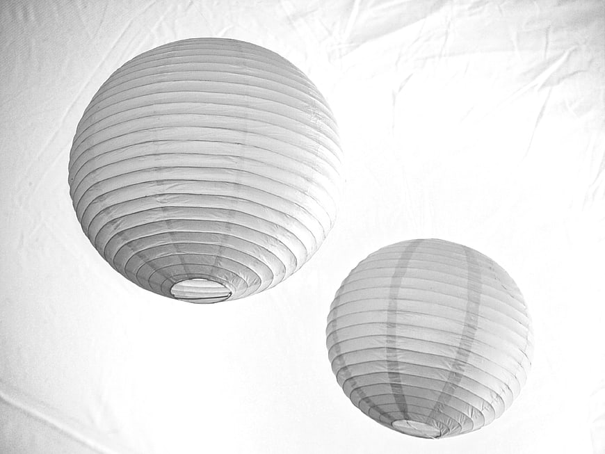 Two white paper lanterns hanging against a textured ceiling background