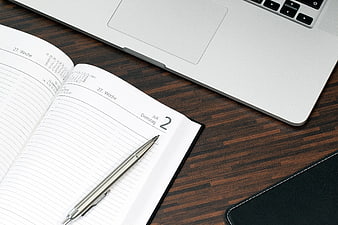 Silver Pen on Open Planner and Laptop on Wooden Desk