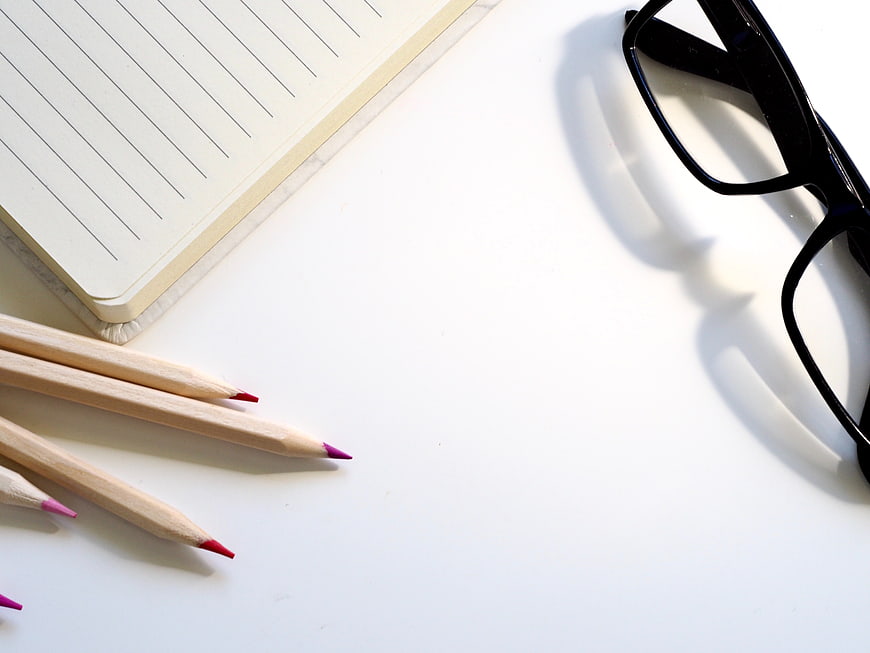 Minimalist workspace with notebook, colored pencils, and glasses