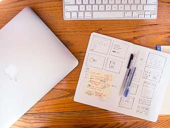 Flat lay of laptop, keyboard, and UX wireframe sketches on wooden desk