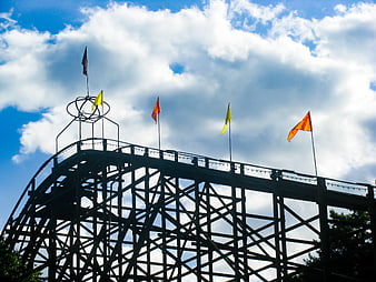 Silhouette of wooden roller coaster with flags against blue sky