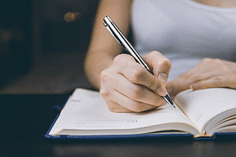 Close-up of woman writing in a planner with a pen