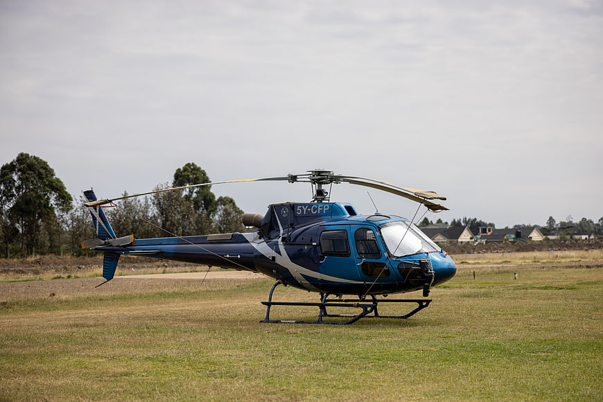Blue helicopter parked on grassy field with registration 5Y-CFP