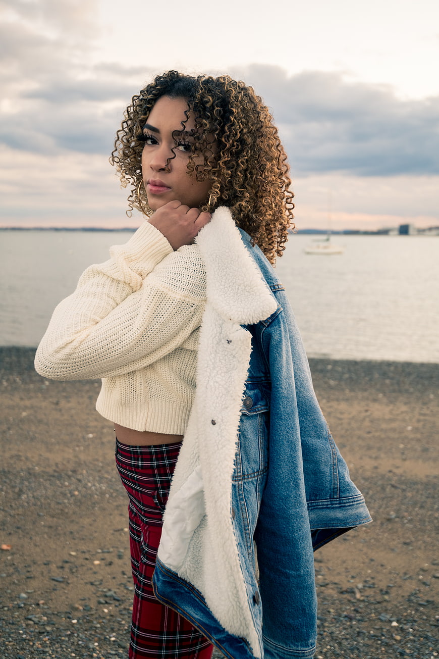 Stylish woman with curly hair on a pebble beach at dusk