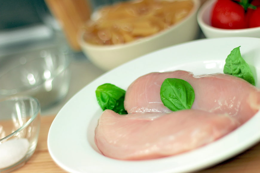 Raw Chicken Breast with Basil Leaves on White Plate