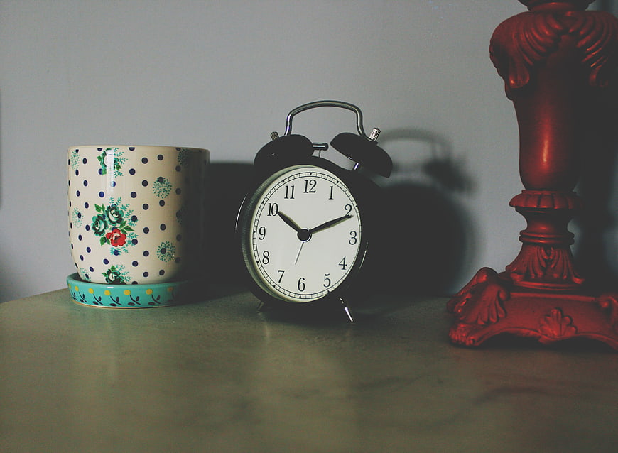 Vintage alarm clock, floral mug, and red lamp on a table