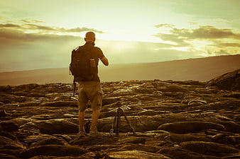 Photographer with tripod on rocky landscape at golden hour sunset