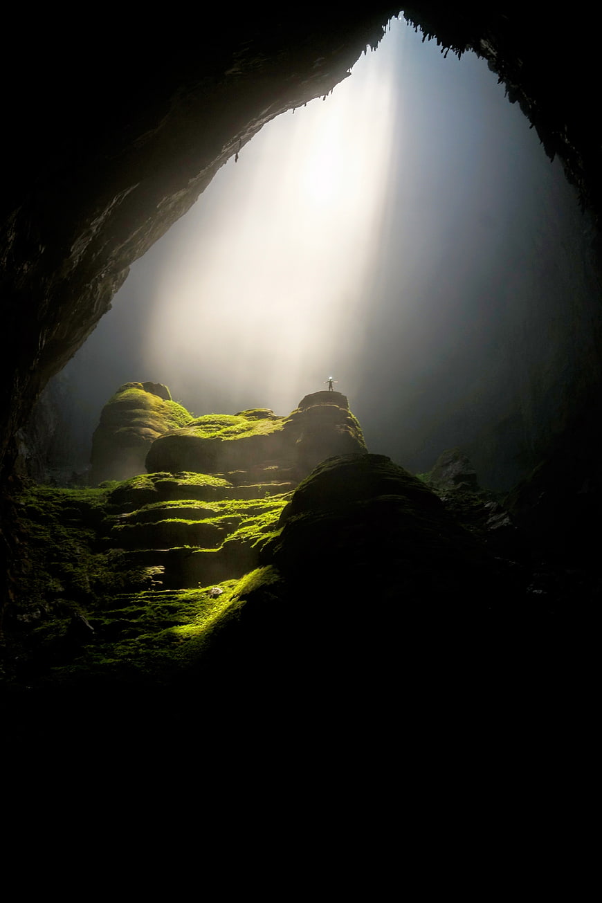 Silhouette of person standing in mossy cave with light rays