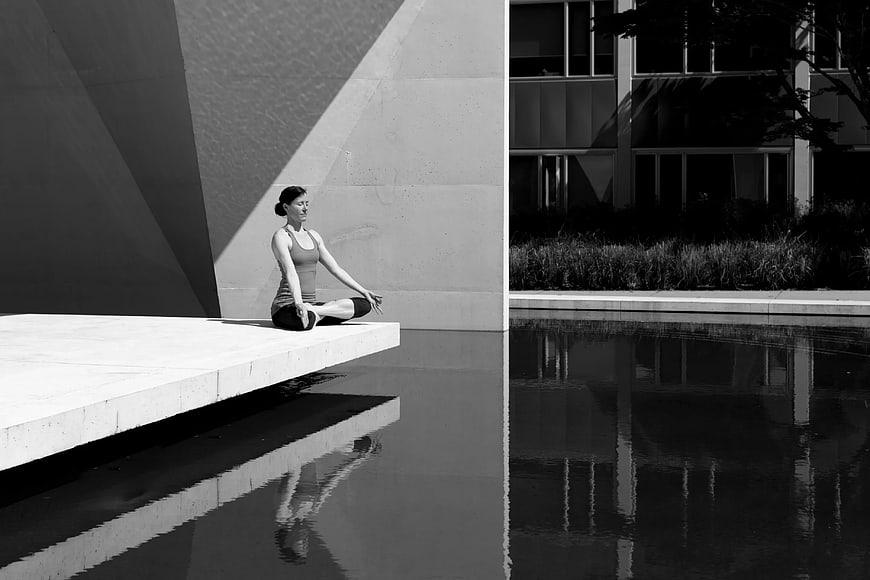 Woman Meditating in Yoga Pose by Modern Architectural Pool
