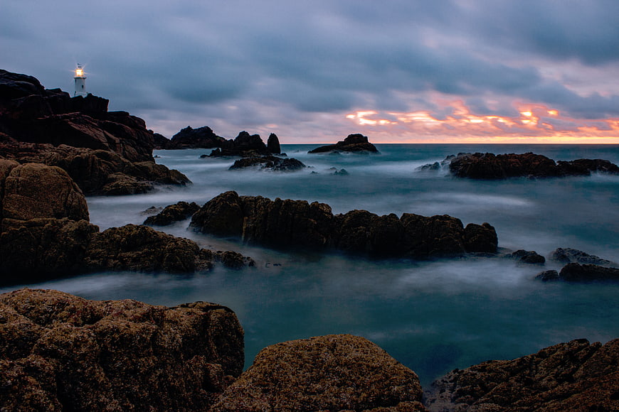 Lighthouse on Rocky Coast at Sunset with Misty Ocean Waves