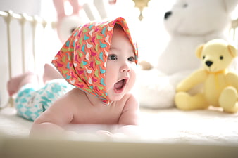 Cute Baby in Colorful Bonnet Lying on Bed with Toys
