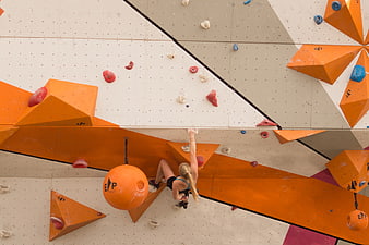Woman bouldering on indoor climbing wall with orange holds