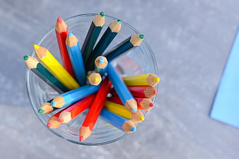 Top view of colorful pencils in a glass cup on gray background
