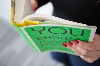Close-up of woman reading motivational book with red nails