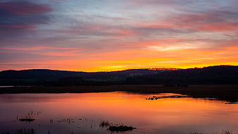 Vibrant Sunset Reflection Over Calm Lake and Silhouette Hills