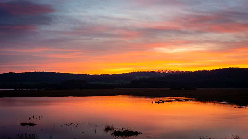 Vibrant Sunset Reflection Over Calm Lake and Silhouette Hills