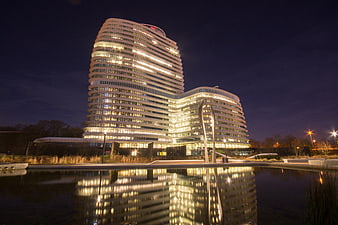 Modern curved office building illuminated at night with water reflection
