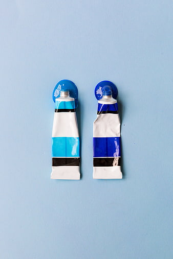 Two blue and white paint tubes on a pastel blue background