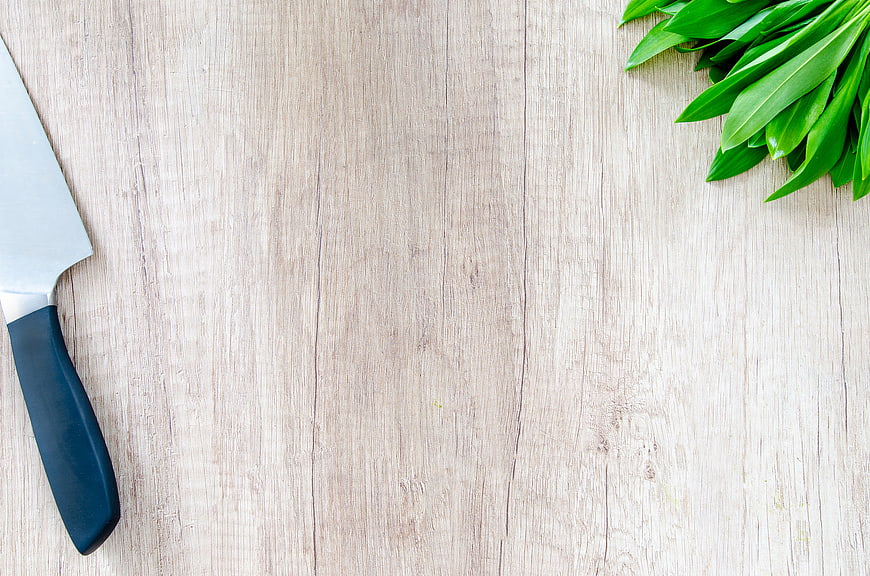 Chef knife and fresh green leaves on light wooden background