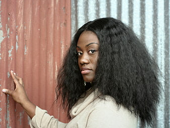 Portrait of young black woman with curly hair against textured wall