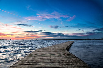 Wooden pier extending into lake at sunset with blue sky