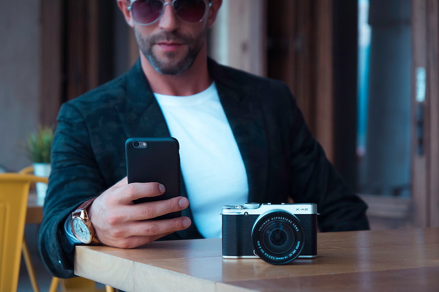 Man with Smartphone and Camera on Wooden Table