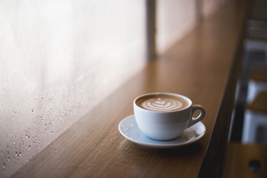 Latte Art Coffee Cup on Wooden Table by Rainy Window