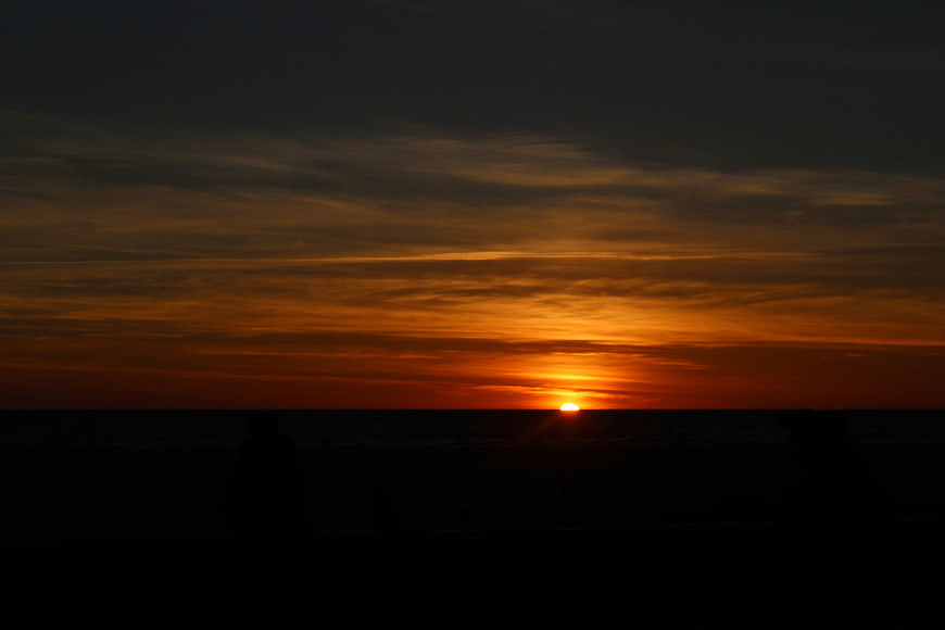 Silhouette of People Watching Orange Sunset Over Ocean Horizon