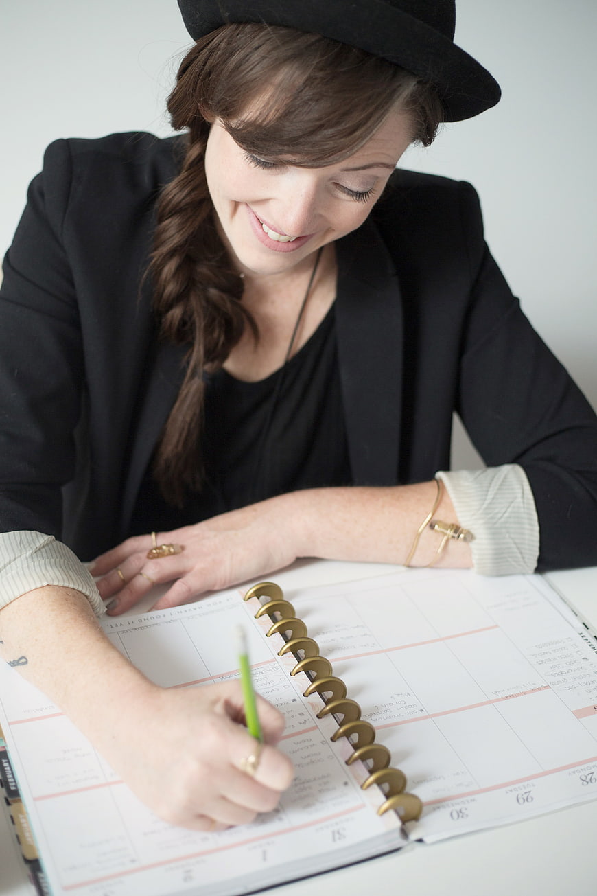 Smiling woman in hat writing in planner