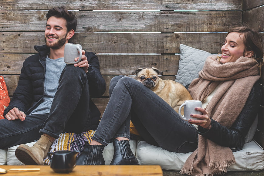 Happy couple relaxing with pug dog and coffee outdoors