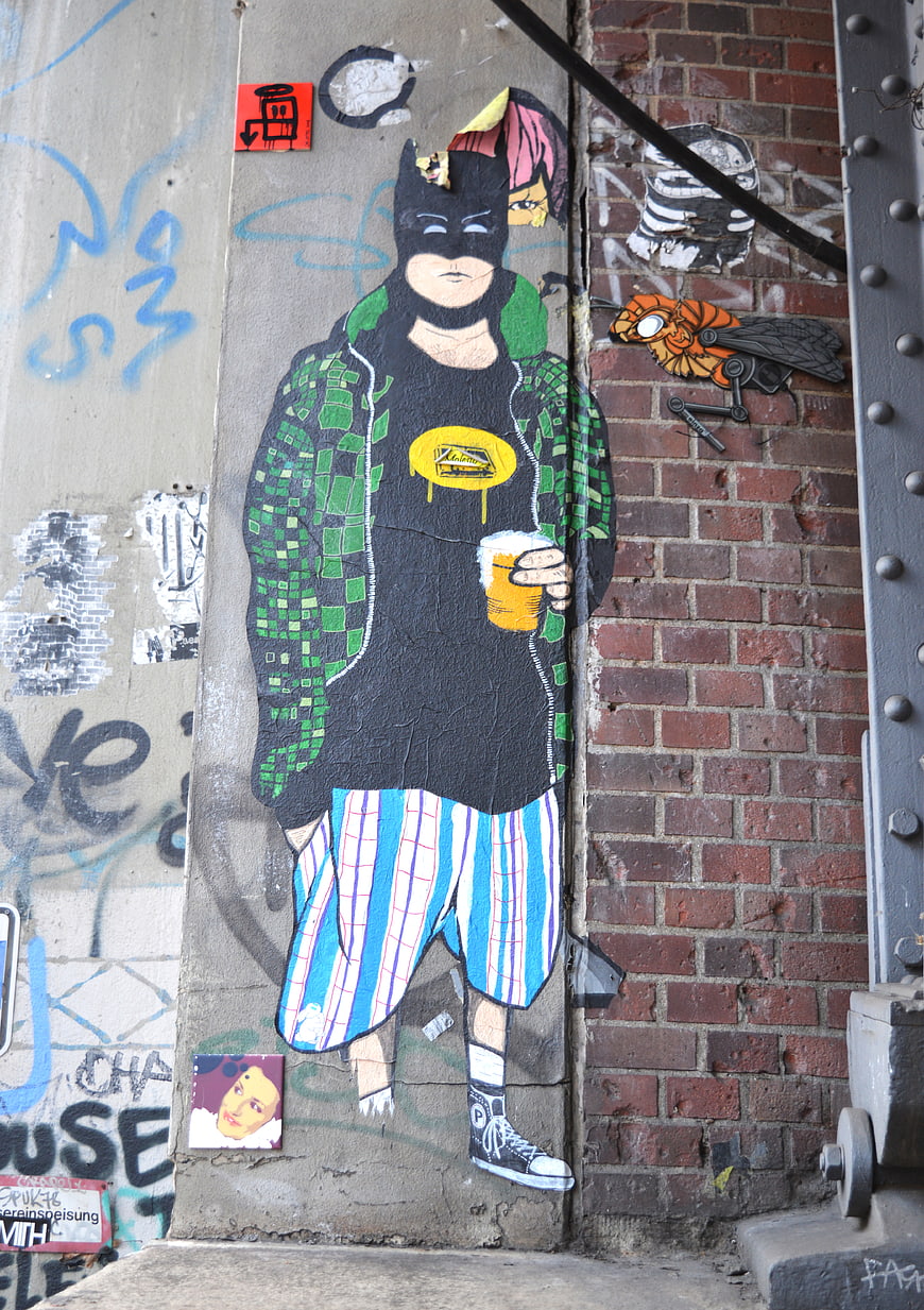 Street art mural of Batman character holding beer on urban wall