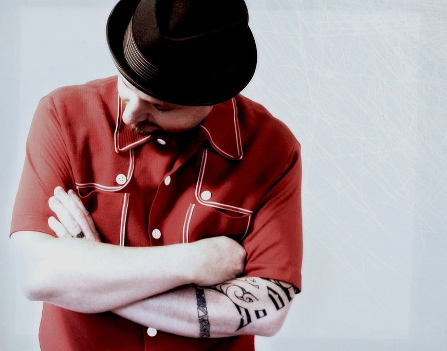 Man in Fedora and Red Shirt with Tattoos Looking Down