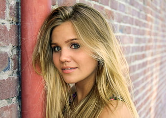 Portrait of young blonde woman leaning against brick wall