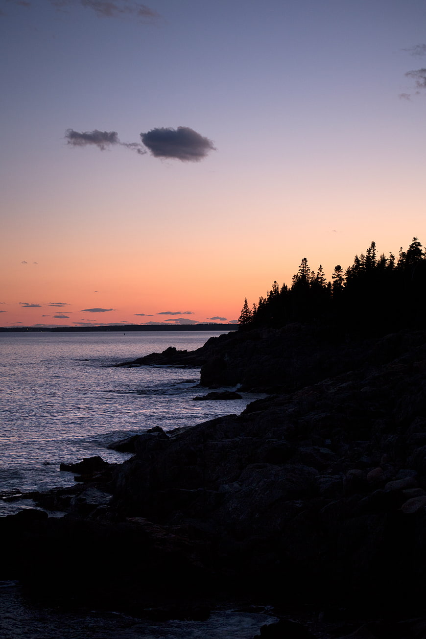 Silhouette of rocky coastline at sunset with orange and purple sky