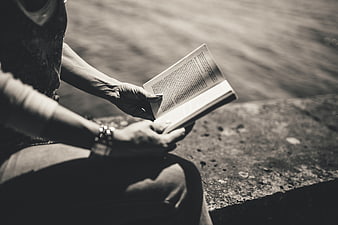 Close-up of hands reading a book outdoors in black and white