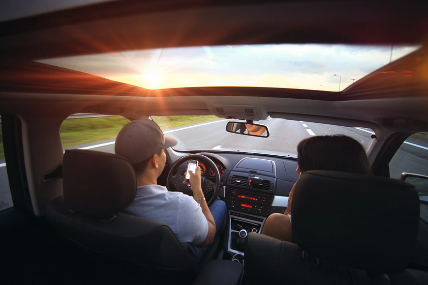 Man Using Smartphone While Driving Car at Sunset