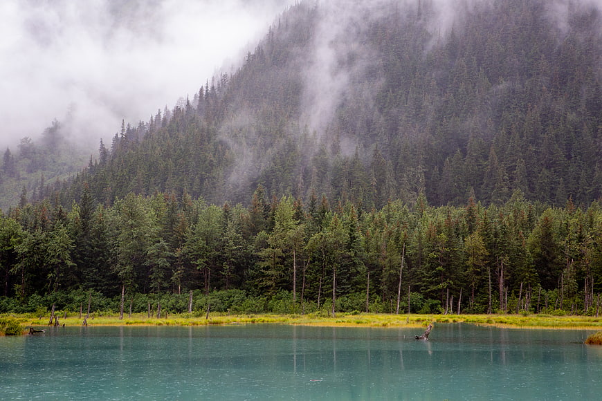 Misty turquoise lake surrounded by dense evergreen forest and mountains