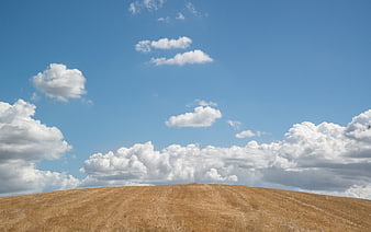 Golden dry grass hill under blue sky with clouds