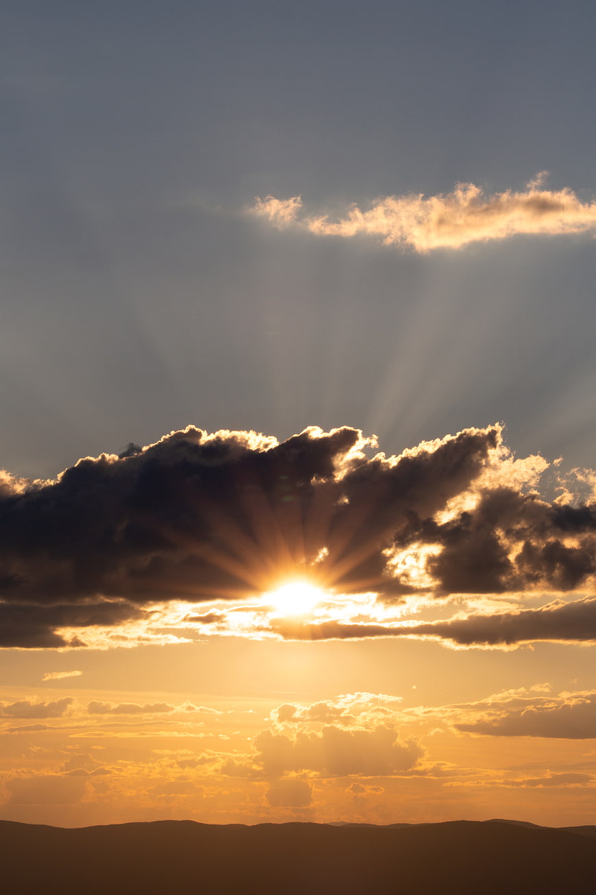 Dramatic Sun Rays Bursting Through Clouds Over Mountain Horizon