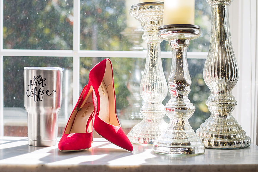 Red heels and coffee tumbler on windowsill with candlesticks