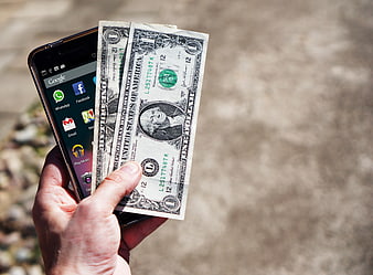 Hand holding smartphone and US dollar bills outdoors