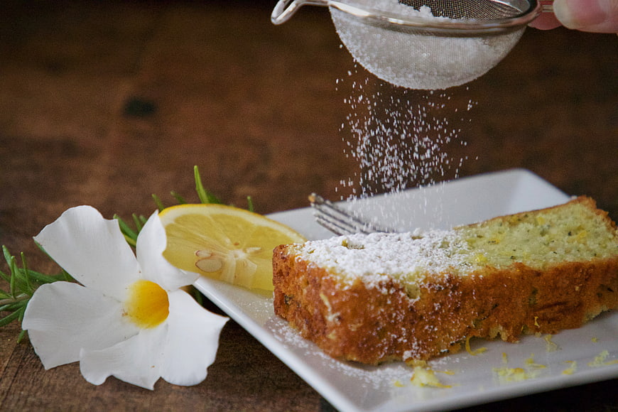 Lemon cake slice being dusted with powdered sugar