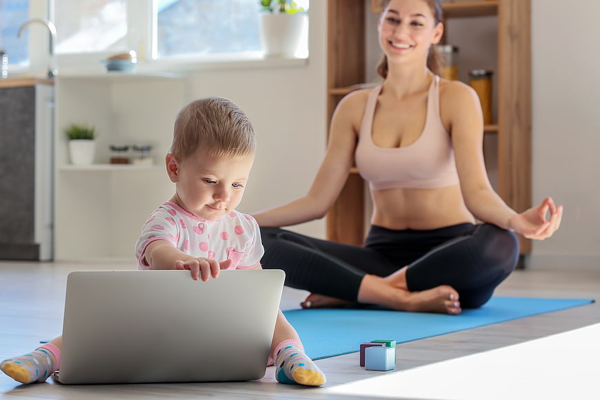 Mother meditating while toddler plays with laptop at home