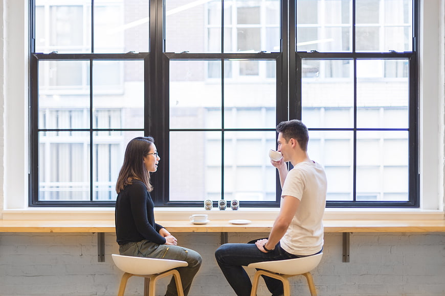 Couple drinking coffee and talking by large window