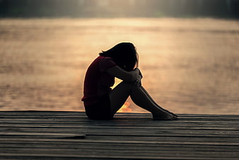 Silhouette of Sad Woman Sitting on Wooden Dock at Sunset