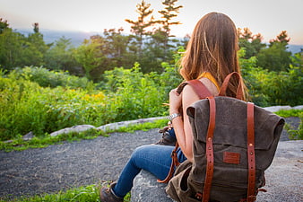 Woman with backpack sitting on rock overlooking nature