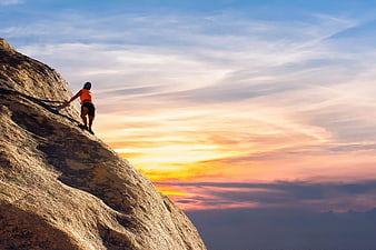 Rock Climber Scaling Mountain Peak at Sunset