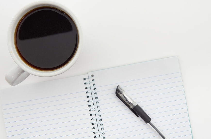 Top View of Coffee Cup, Notebook, and Pen on White Desk