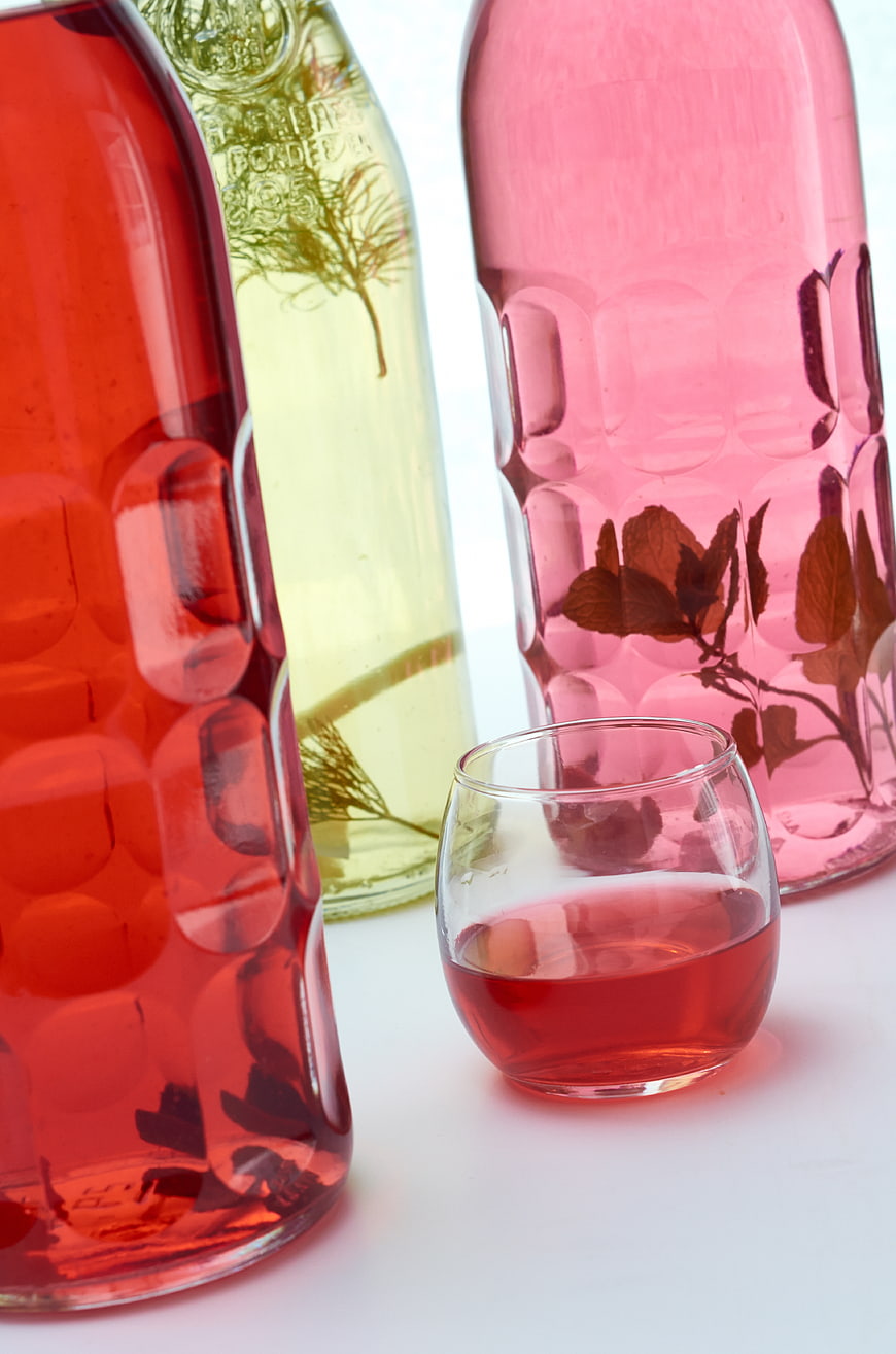 Colorful Infused Spirits in Glass Bottles with Herbs
