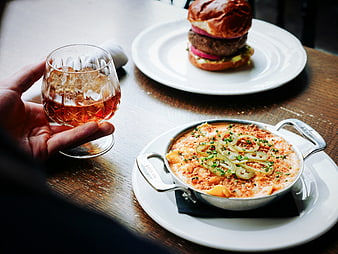 Hand holding cocktail with burger and mac and cheese on wooden table